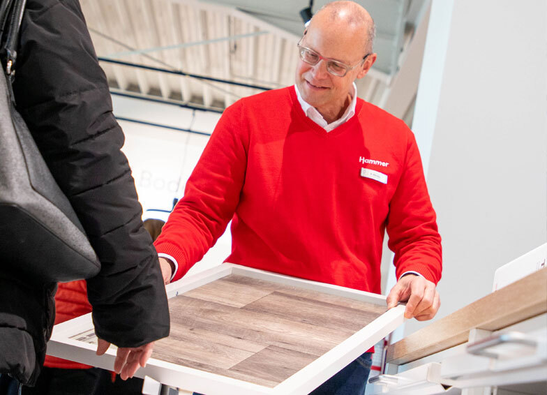 Hammer Fachmarkt: Das Bild zeigt einen Hammer-Mitarbeiter in roter Kleidung, der einem Kunden einen Bodenbelag präsentiert.